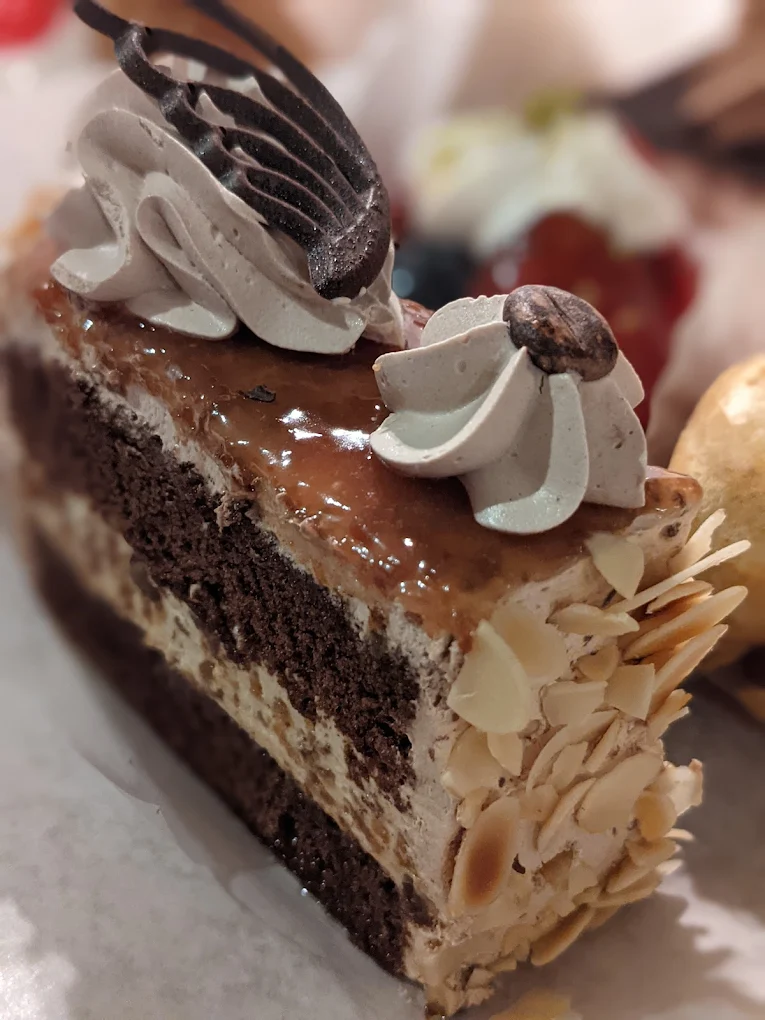 Gourmet layered cake slice with glossy glaze, almond sides, and coffee bean garnish