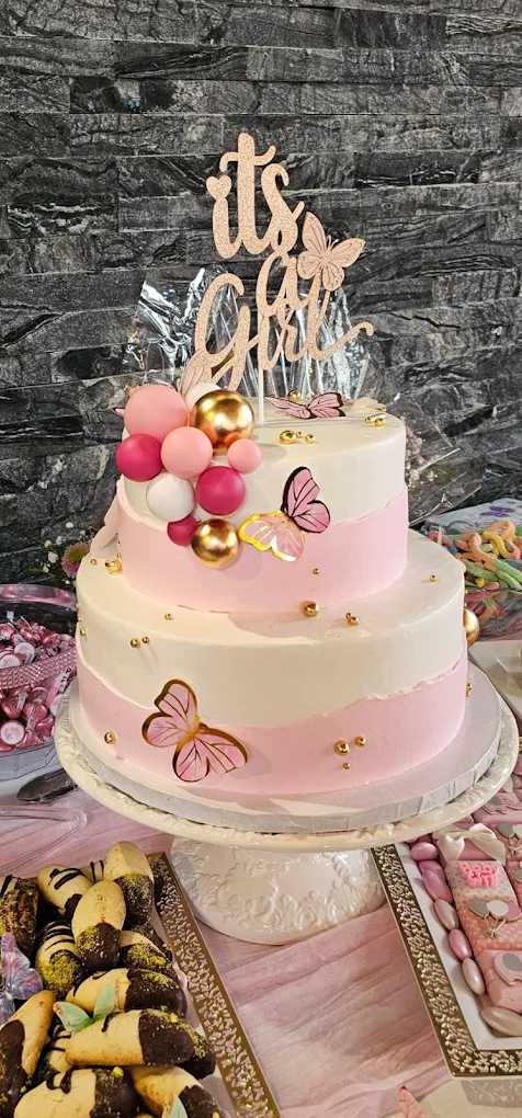 Pink and white two-tier cake with butterflies, pearls, and It is a Girl topper